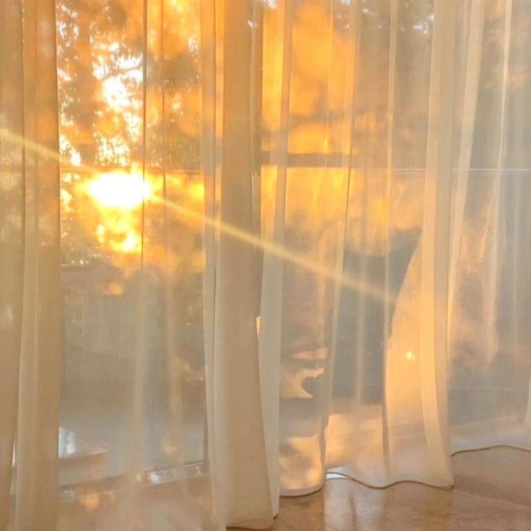 Warm golden sunlight streams through sheer white curtains, casting a soft glow and creating a peaceful, sunlit atmosphere.