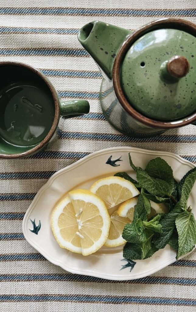 Green ceramic teapot with lemon slices and fresh mint on a striped cloth, representing soothing herbal teas and mindful nutrition for IC-friendly diets