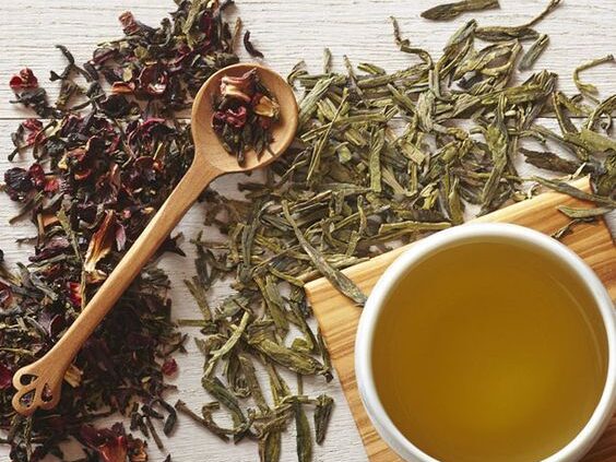 Cup of herbal tea with loose green and hibiscus leaves on a wooden surface, illustrating soothing caffeine-free options for bladder comfort in IC.
