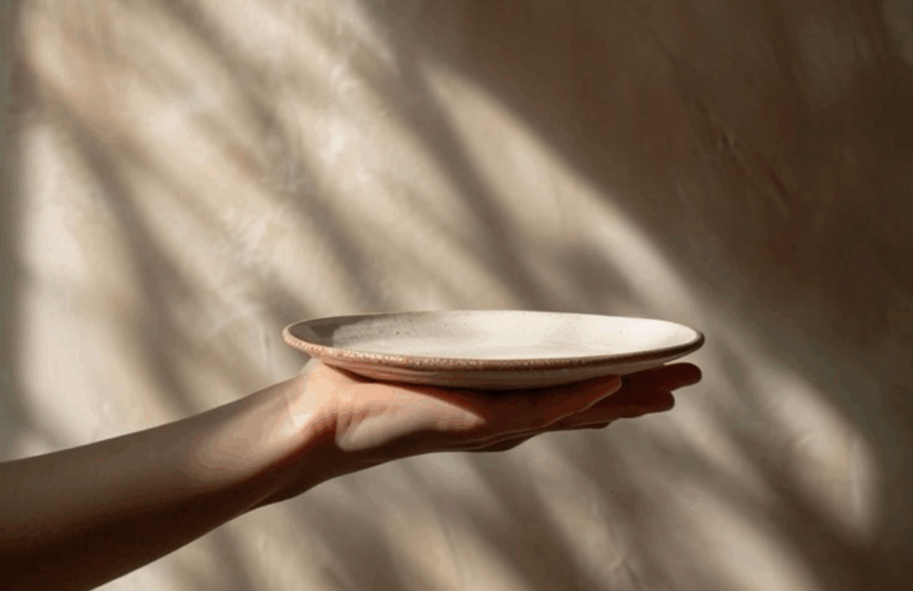 A hand gently holding an empty ceramic plate in warm natural light, representing mindful food choices and awareness of dietary triggers for interstitial cystitis.