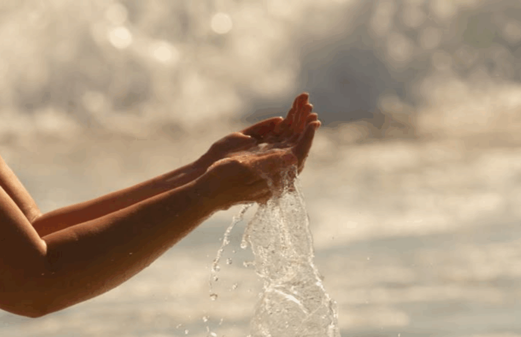 Hands cupping flowing water at the shoreline, illustrating calm, grounding, and nervous-system regulation strategies for managing IC flares.