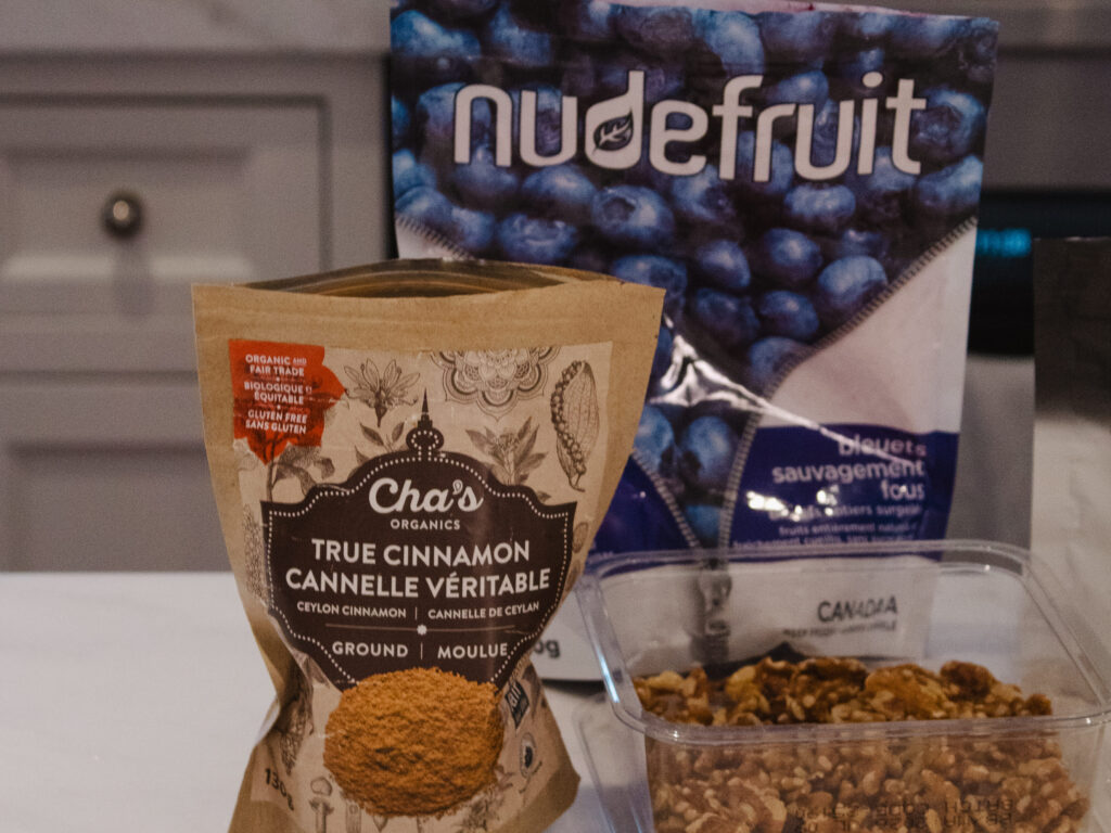 Ingredients for a healthy daily smoothie including wild blueberries, cinnamon, walnuts, flax seeds, and protein powder on a kitchen counter.