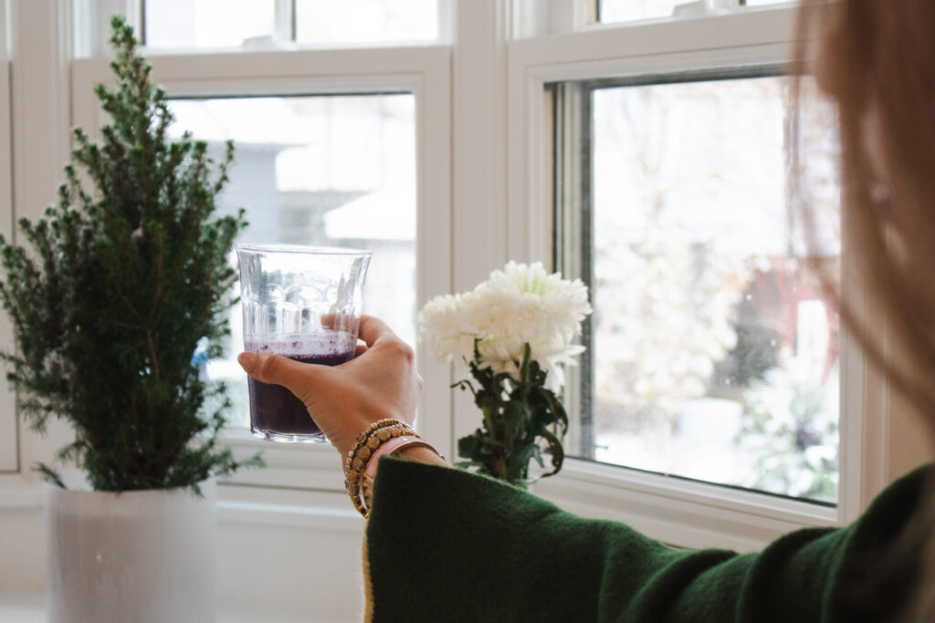Woman holding a glass of wild blueberry healthy daily smoothie near a window in natural light.