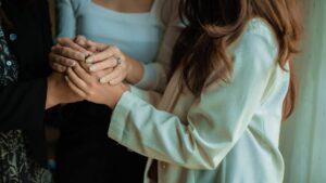 Close-up of two people gently holding hands in a supportive, comforting gesture, with soft natural lighting and neutral-toned clothing.