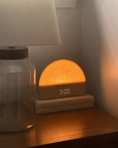 Warmly lit bedside table with a glowing digital clock displaying 3:00 AM, symbolizing nighttime awakenings, insomnia, and disrupted sleep.