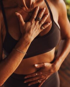 Person placing one hand over their chest and the other on their lower abdomen, representing the mind-body connection, stress, and women's hormonal health.