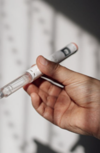 Close-up of a hand holding a white injectable medication pen, with a blurred background.