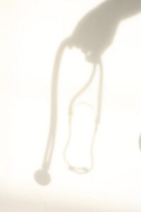 Soft, sunlit shadow of a stethoscope cast against a warm, neutral background.