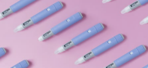 Multiple blue injectable medication pens arranged diagonally on a pink background.