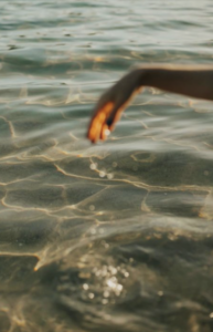 A hand gently skimming the surface of sunlit, clear water with golden reflections.