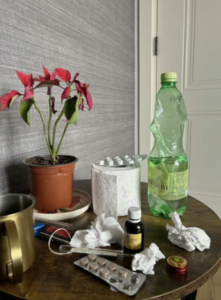Table covered with tissues, medication packages, a drink bottle, and other sick-day essentials, representing frequent illness during cold and flu season.