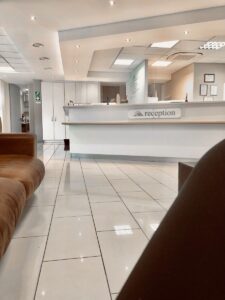 Bright medical clinic reception area with a white front desk and comfortable waiting room seating, representing the importance of preparing questions, symptoms, and priorities before a doctor's appointment.