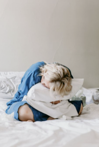 Woman curled up on a bed holding a pillow, representing the pain, fatigue, and daily impact that can be associated with endometriosis.