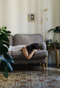Woman lying exhausted on a couch with her head resting on her arms, representing persistent fatigue, low energy, and the impact of exhaustion on daily life.
